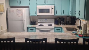Una cocina con gabinetes color turquesa, un refrigerador blanco, un microondas, una estufa y una cafetera.