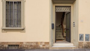 Ein Gebäudeeingang mit einer Treppe, einem Fenster mit Fensterläden und einem kleinen Schild an der Wand.