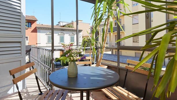 Ein Balkon mit rundem Tisch, einer Bank und einem Blumentopf.