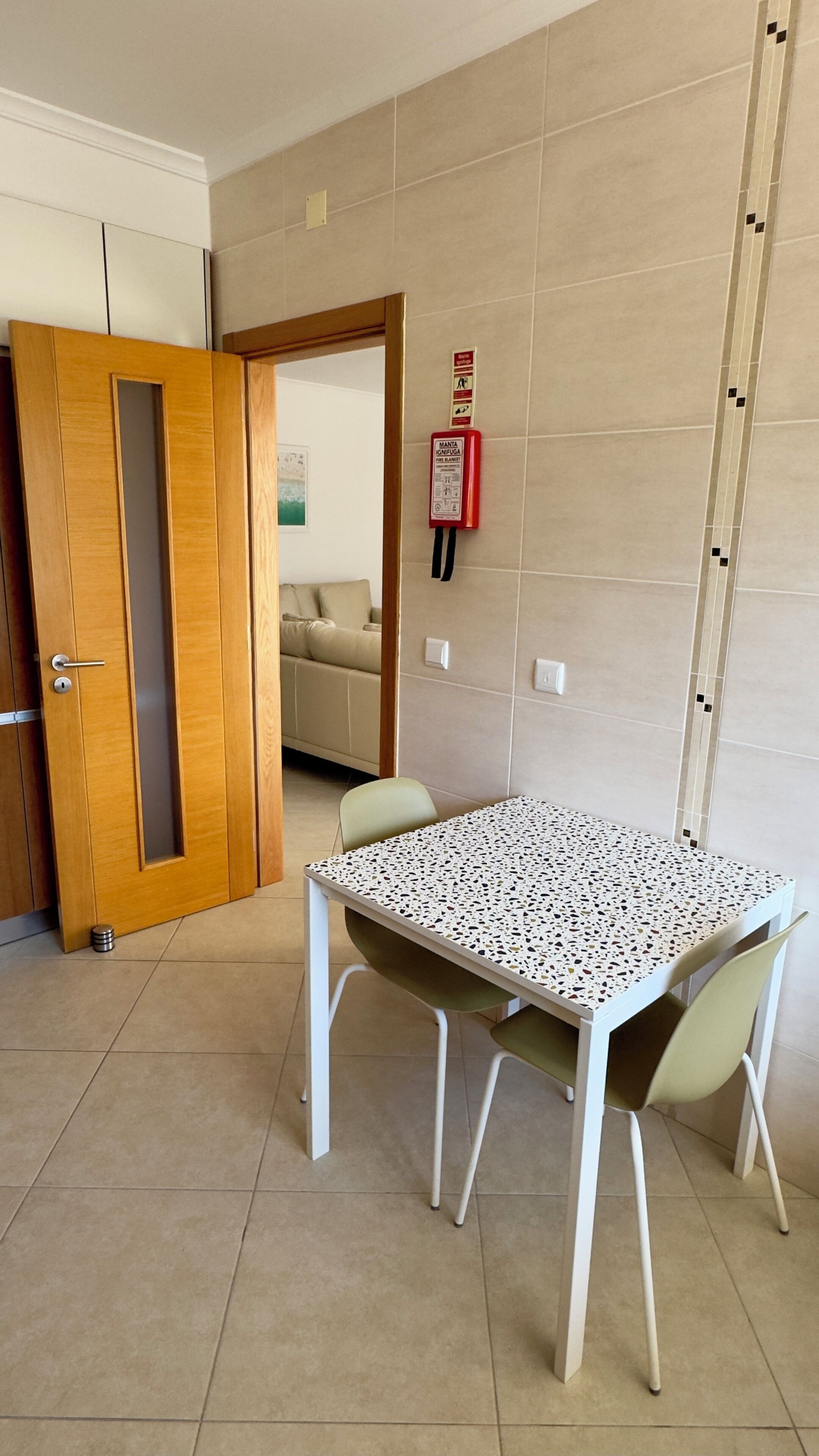 A room with a wooden door, a table with a speckled top, and a fire extinguisher on the wall.