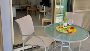 Uma mesa de vidro com cadeiras, uma garrafa de vinho e copos em um suporte.