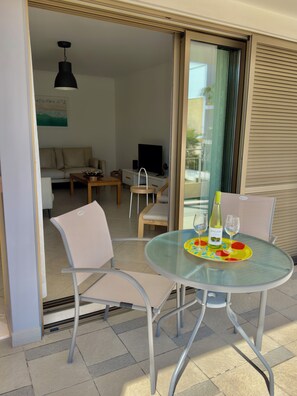 A glass table with chairs, a bottle of wine, and glasses on a tray.