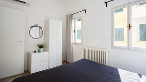 A bedroom with a bed, a wardrobe, a radiator, and a window with shutters.