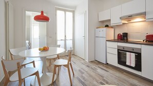 A modern kitchen with white cabinets, a red hanging light, and a dining area with a round table and wooden chairs.