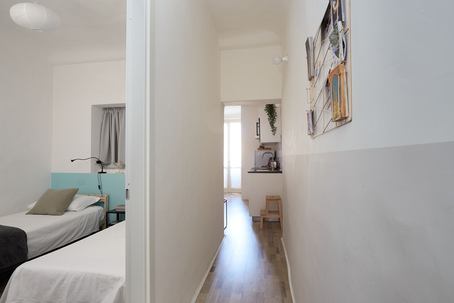 A narrow hallway with a bed on the left, a small kitchenette on the right, and a door leading to another room.