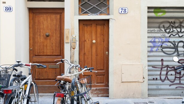 A wooden door with a window above it, a garage door with graffiti, and two bicycles parked in front.