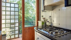 Une cuisine équipée d’une cuisinière à gaz, de carreaux blancs et d’une fenêtre donnant sur un paysage verdoyant.