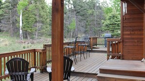 Una terraza de madera con mobiliario exterior, incluyendo sillas y mesas, con vistas a una zona boscosa.