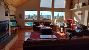 Amplia sala de estar con techos altos, grandes ventanales que ofrecen vistas al exterior, chimenea y diversas opciones de asientos.