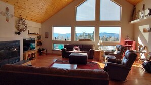 Amplia sala de estar con techo alto, ventanas grandes que ofrecen vistas a la montaña, chimenea y un rincón de estar acogedor.