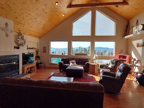 A spacious living room with a high ceiling, large windows offering mountain views, a fireplace, and a cozy seating area.