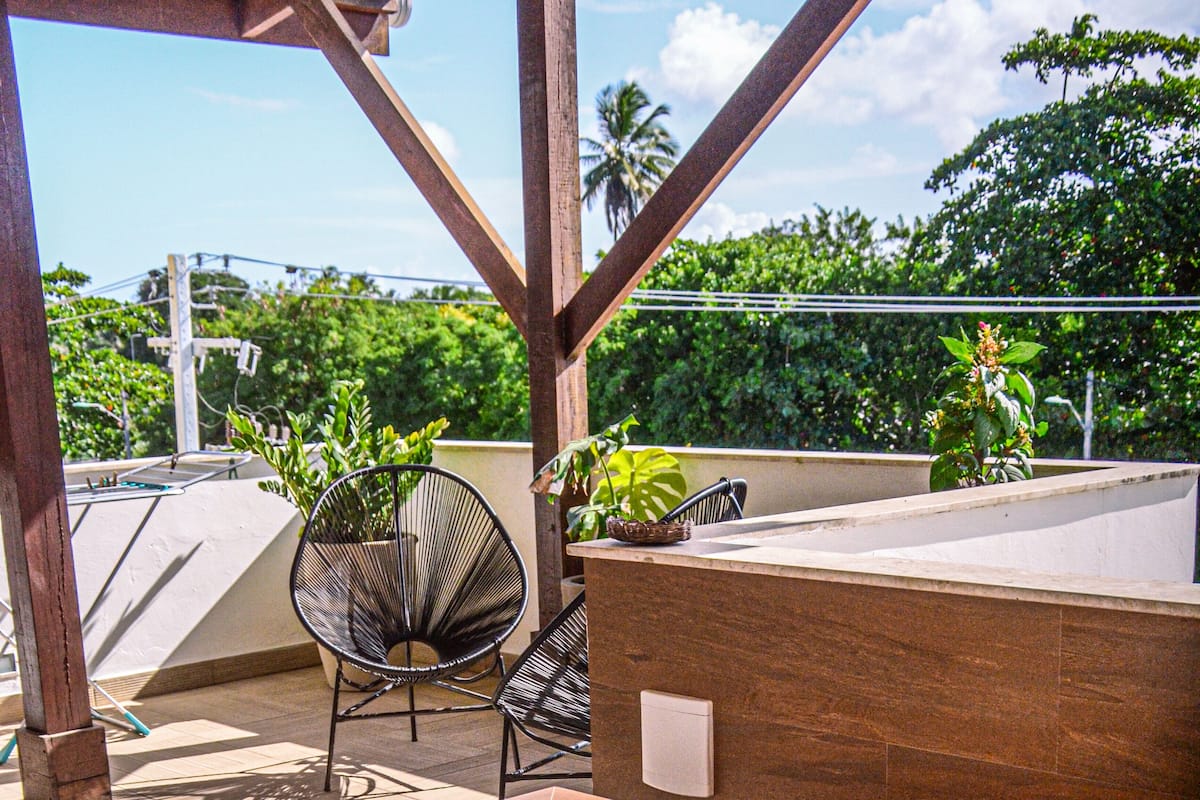 A hot tub with a wooden pergola overhead, surrounded by chairs and potted plants.