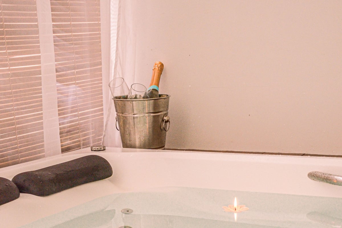 A spa bath with a glass floor, a candle, and a metal bucket with a bottle.
