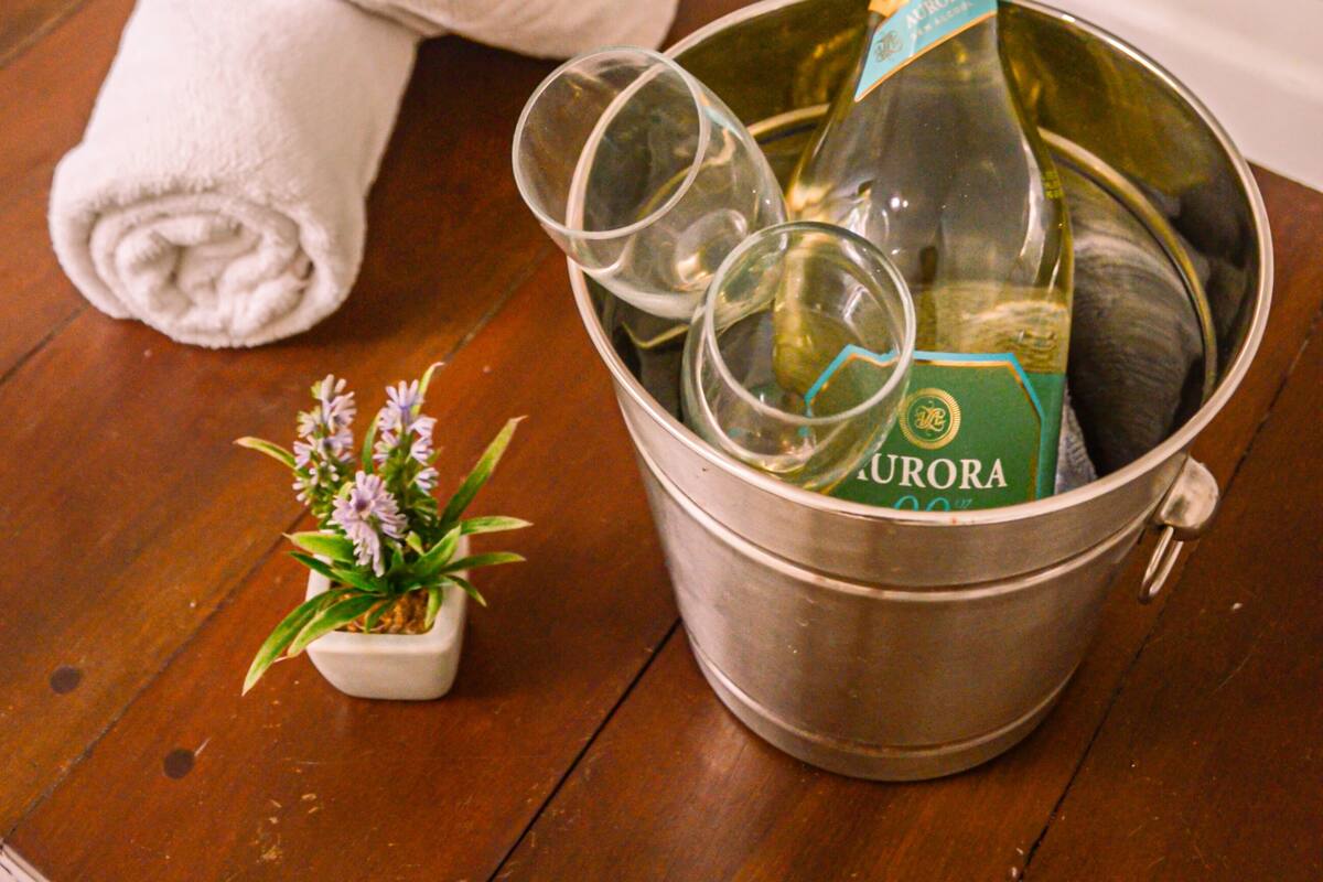 A bucket with a bottle of champagne, glasses, a rolled towel, and a small potted plant on a wooden floor.