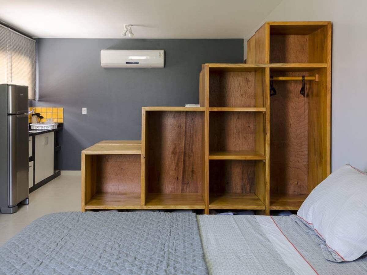 Una habitación compacta con cama, kitchenette y estanterías de madera empotradas.