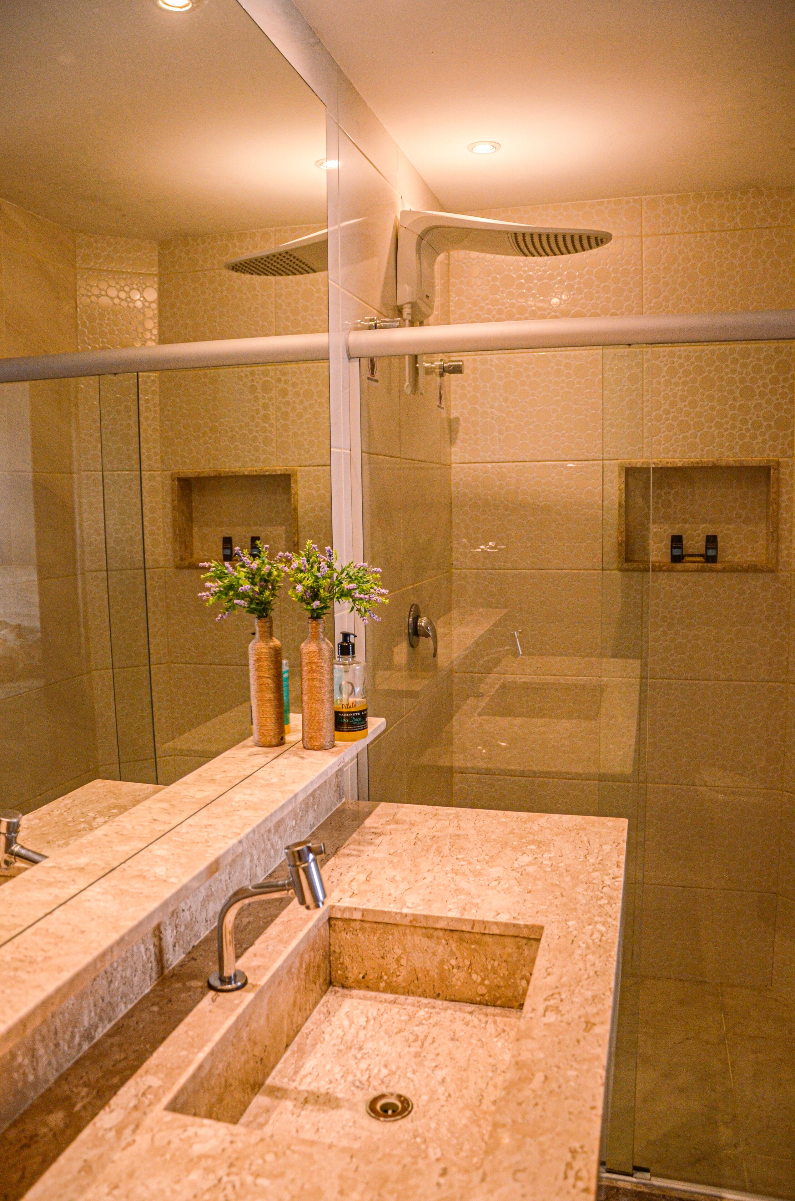A modern bathroom with a glass-enclosed shower, a marble sink, and two vases with flowers.
