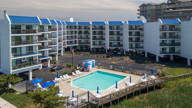 A modern hotel with multiple balconies, a swimming pool, and a parking area. - Bay Princess renovated and decorator furnished, bayfront condo in convenient midtown location (OCEAN CITY)