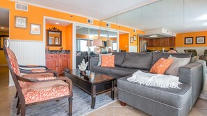 A living room with a grey sofa, orange cushions, a wooden coffee table, and a patterned rug. - Bay Princess renovated and decorator furnished, bayfront condo in convenient midtown location (OCEAN CITY)