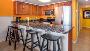 A kitchen with wooden cabinets, a granite countertop, a stainless steel refrigerator, and a microwave. - Bay Princess renovated and decorator furnished, bayfront condo in convenient midtown location (OCEAN CITY)
