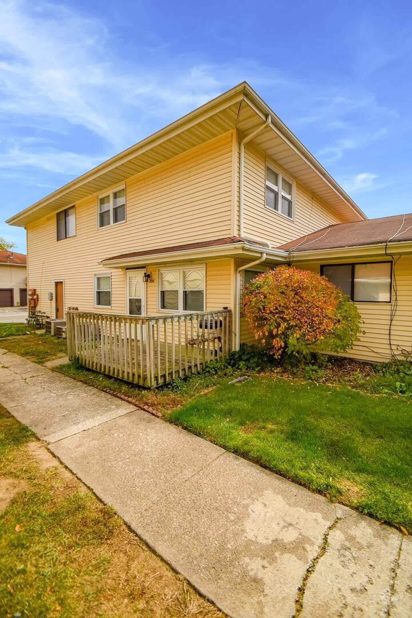 A two-story residential building with a front porch, a small front yard, and a sidewalk leading to the entrance.