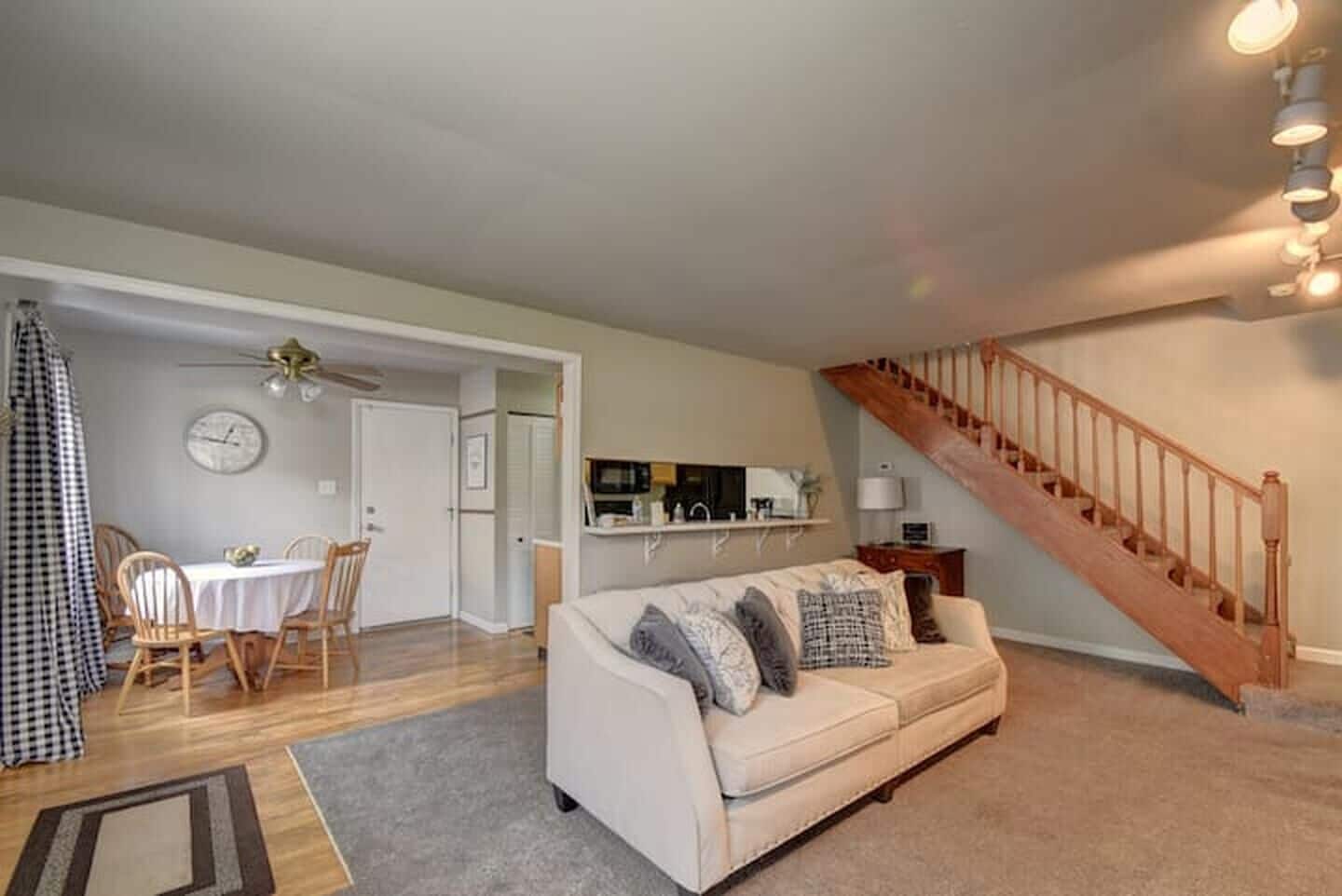 A living room with a sofa, a dining table with chairs, a kitchen area, and a staircase.