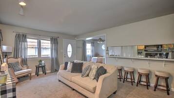 A living room with a beige sofa, a coffee table, and a dining area with a kitchen in the background.