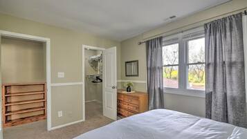 A bedroom with a bed, a walk-in closet, a dresser, and a window with curtains.