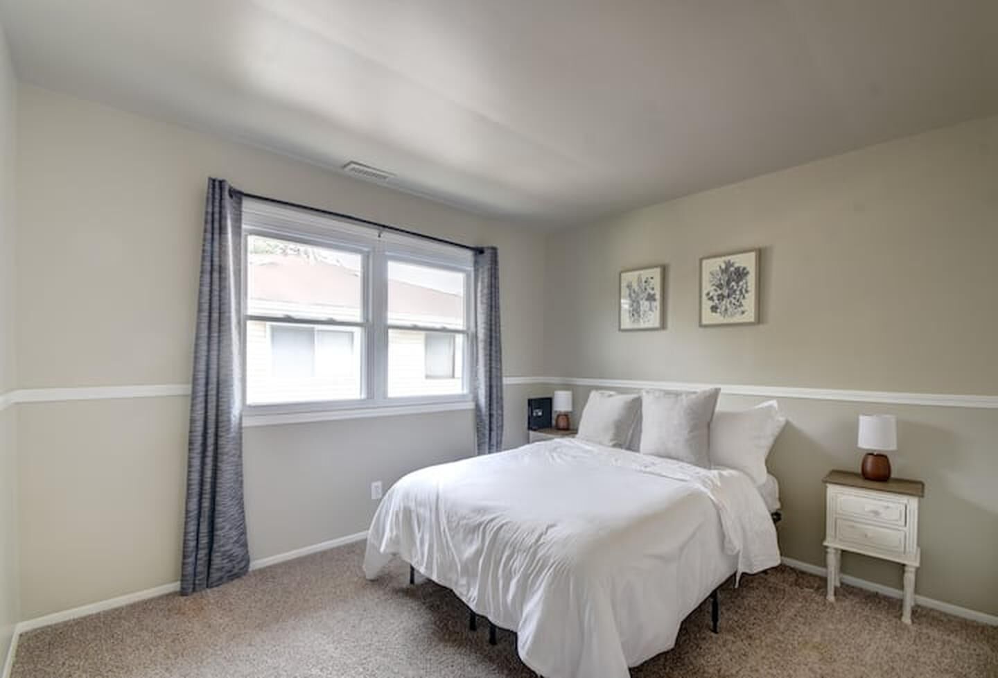 A bedroom with a bed, a nightstand, a lamp, and two wall-mounted picture frames.