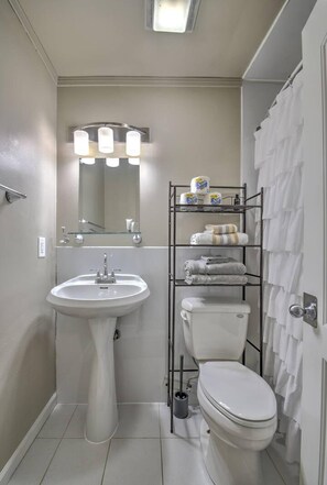Ein Badezimmer mit einem Standwaschbecken, Toilette, Ablage für Handtücher und einem beleuchteten Spiegel.