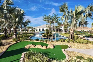 A golf course with a putting green, a swimming pool, and palm trees.