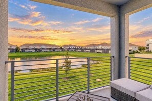 A balcony with a view of a residential area and a body of water during sunset.