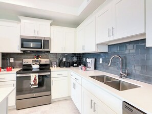 A modern kitchen with white cabinetry, a stainless steel oven, a microwave, and a double sink.