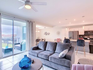 A modern living room with a grey sofa, a dining area, and a kitchen.
