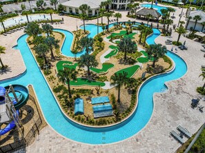 A large swimming pool with multiple lanes and a water slide, surrounded by palm trees and lounge chairs.