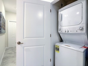 A laundry room with stacked washers and dryers, a door, and a hallway with a door.
