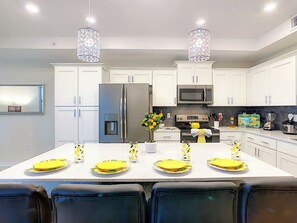 A modern kitchen with white cabinets, stainless steel appliances, and a central island with yellow plates and glasses.