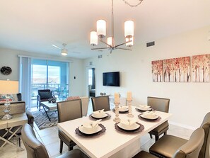 A dining area with a white table set for six, a ceiling fan, and a TV mounted on the wall.