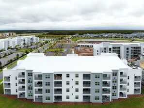 A multi-story residential building with a flat roof, a parking lot, and a landscaped area with trees.