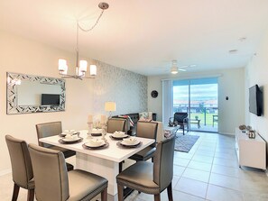 A dining area with a white table set for four, surrounded by chairs, a chandelier, and a large mirror on the wall.