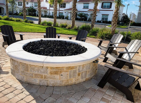 A circular stone fire pit with seating around it, set on a paved patio.