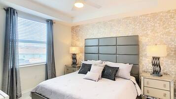 Een slaapkamer met een groot bed, twee nachtkastjes, een plafondventilator en een raam met gordijnen.