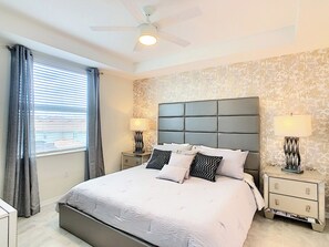 A bedroom with a large bed, two bedside tables, a ceiling fan, and a window with curtains.