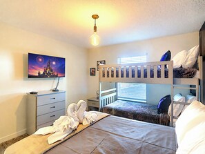 A bedroom with bunk beds, a desk, a chair, a flat-screen TV, and a wall-mounted light fixture.