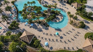 Vista aérea de un resort con una gran piscina, tumbonas y palmeras.
