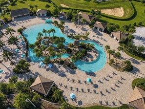 Luchtbeeld van een resort met een groot zwembad, ligbedden en palmbomen.