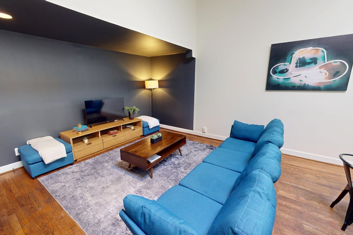 A modern living room with a sectional sofa, a wooden entertainment unit, a flat-screen TV, and a floor lamp.