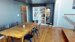 Un comedor con una mesa y sillas de madera, una pared de ladrillo y una estantería blanca con diversos objetos.