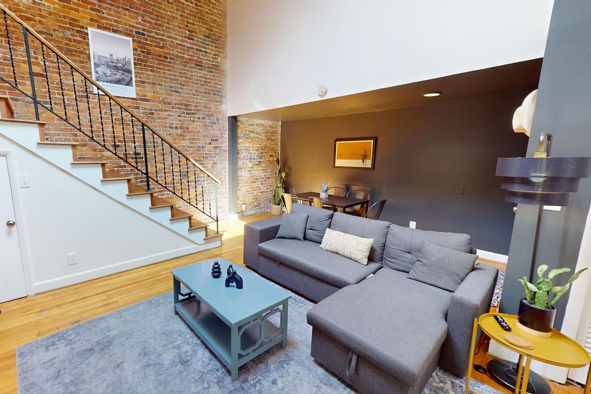 A modern living room with a staircase, grey sofa, coffee table, and a guitar.