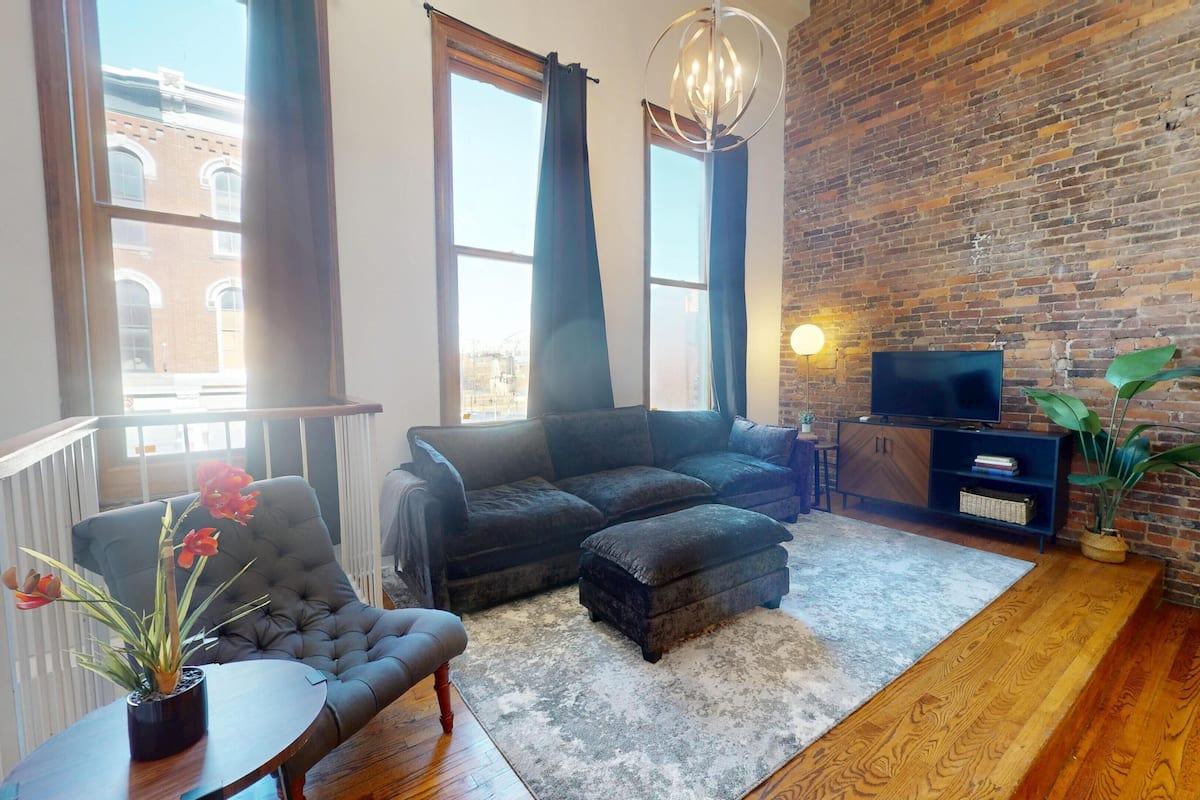 A modern living room with a brick wall, a sofa, a TV, and a potted plant.