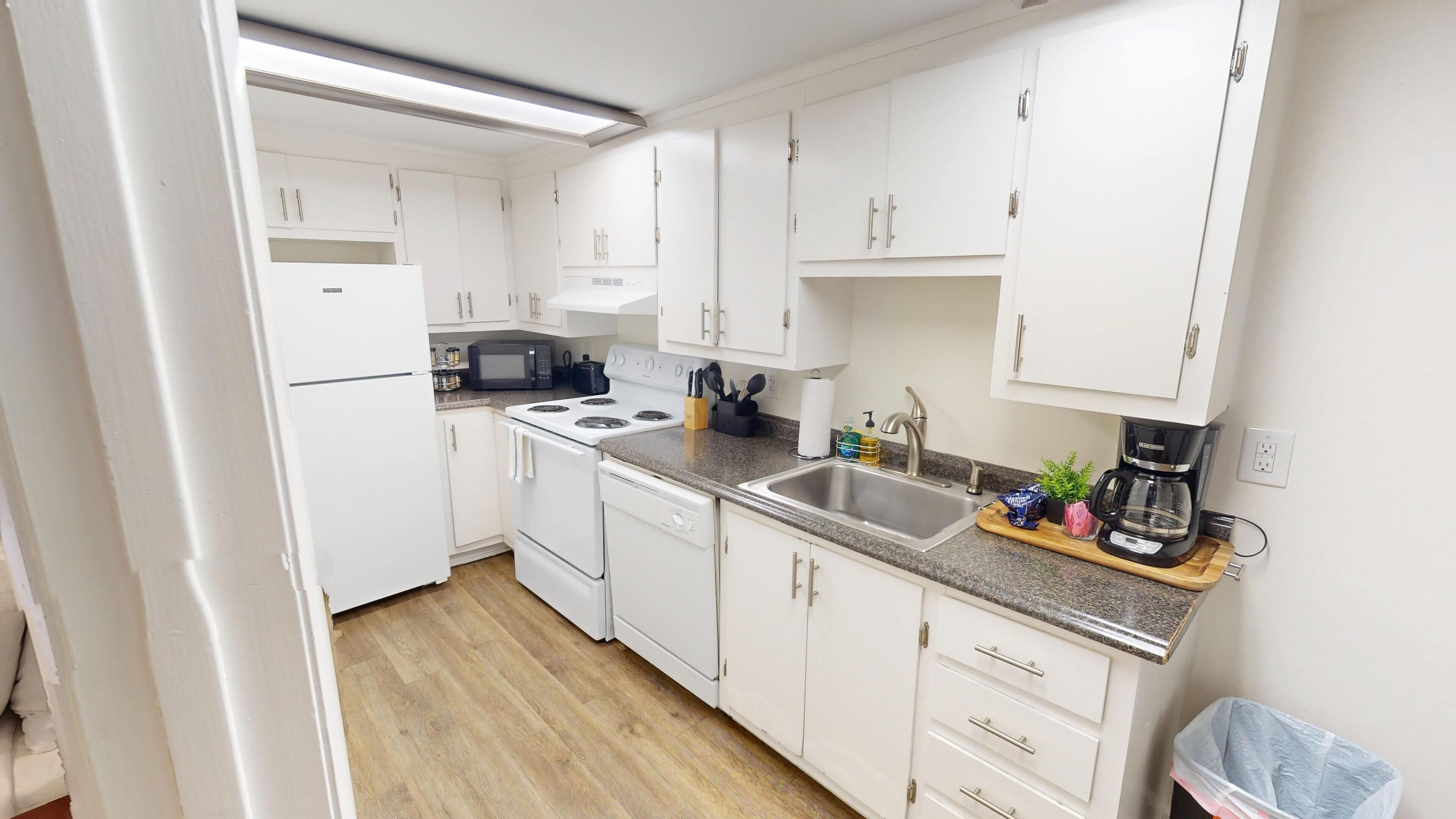 A modern kitchen with white cabinetry, a stainless steel sink, and a coffee maker.